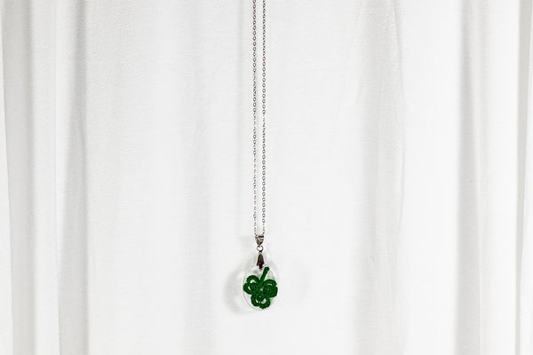 Majhen ovalen obesek iz epoksidne smole z zeleno triperesno deteljo iz čipke. Visi na krajši verižici iz medenine oz. bakra.