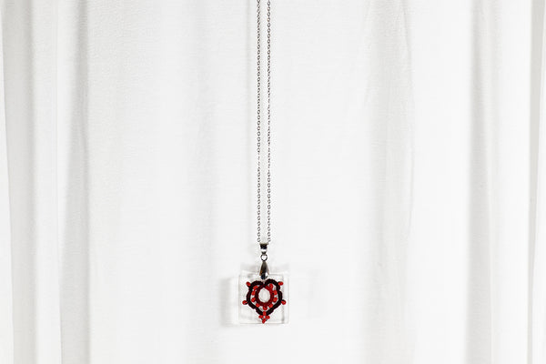 Manjši obesek kvadratne oblike iz epoksidne smole, s čipko temno rdeče prelivajočega javorjevega lista s perlami. Visi na krajši verižici iz medenine oz. bakra.