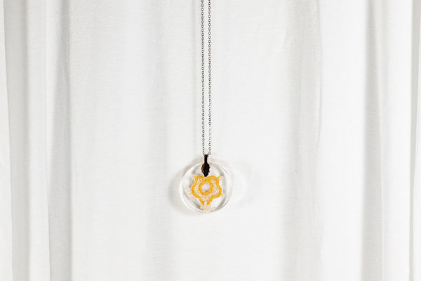 Okrogel obesek iz epoksidne smole, s čipko v obliki javorjevega lista s perlami, v barvah temno rumene in svetlo zelene. Visi na krajši verižici iz medenine oz. bakra.