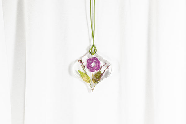 Prekrasen obesek baročne oblike iz epoksidne smole, s ciklamno vijoličnim cvetom iz čipke  ter sušenim zelenjem. Visi na zeleni usnjeni vrvici.