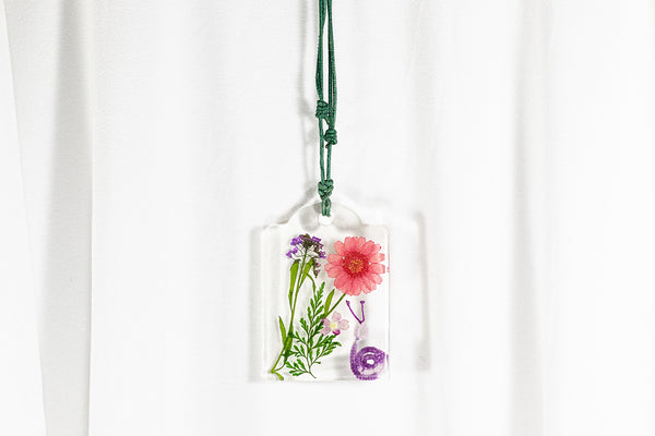Obesek iz epoksidne smole z vijolično belim polžem iz čipke ter sušenim vijolično rdečim cvetjem. Visi na temno zeleni vrvici iz povoščenega bombaža.
