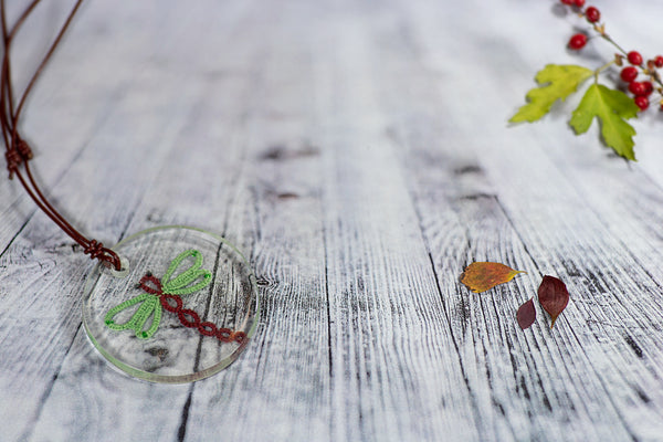 Večji okrogel obesek iz epoksidne smole, z zeleno rdečim kačjim pastirjem, ki visi na usnjeni temno rdeči vrvici.