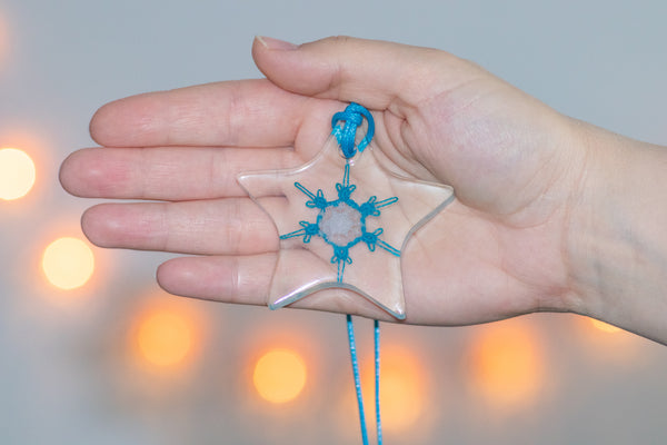 Večji obesek zvezdaste oblike iz epoksidne smole, s svetlo modro čipkasto snežinko ter belo snežinko iz polimerne smole na sredini. Visi na svetlo modri vrvici iz povoščenega bombaža.