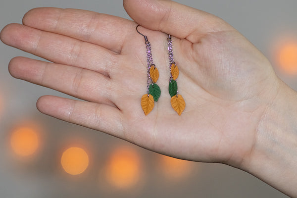 Viseči uhani treh lističev iz polimerne gline v različnih kombinacijah barv, ki visijo na verižicah iz medenine oz. bakra. Kaveljčki so iz nerjavečega jekla.