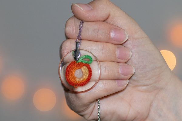 Okrogel obesek iz epoksidne smole z oranžno rumeno pomarančo iz čipke. Visi na krajši verižici iz medenine oz. bakra.