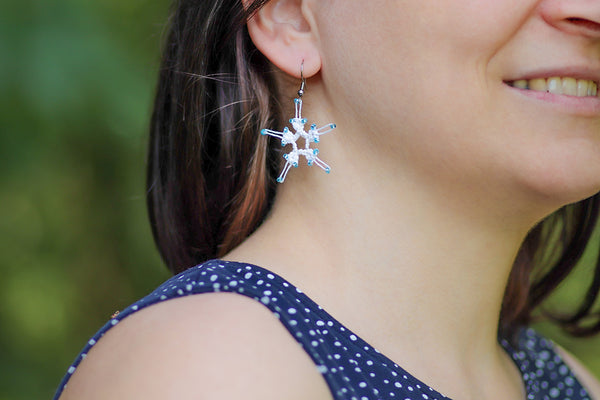 Viseči uhani v obliki bele snežinke s svetlo modrimi perlami. Uhani visijo na nastavkih iz nerjavečega jekla.