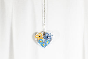 HEART-SHAPED PENDANT WITH A BLUE AND YELLOW BUTTERFLY ON FORGET-ME-NOT FLOWERS