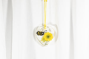 Obesek iz epoksidne smole v obliki srca, na daljši bombažni vrvici rumene barve, v katerem je čebela iz čipke na pravem sušenem rumenem cvetju.