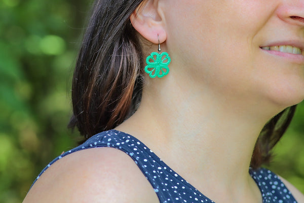Čipkasti viseči uhani v obliki štiriperesne detelje na izbiro v dveh odtenkih zelene, ki visijo na kaveljčkih iz nerjavečega jekla.